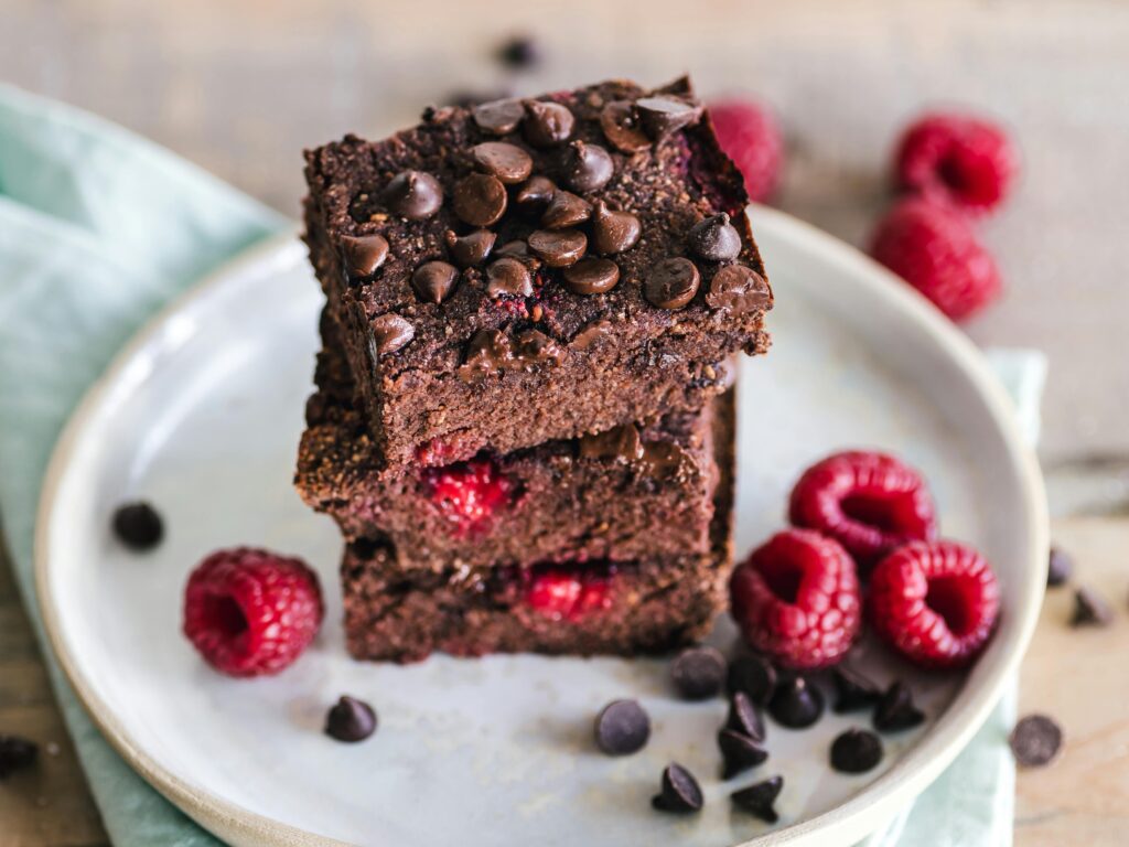 pexels photo 3026804 3026804 Close-up of deliciously indulgent chocolate raspberry brownies stacked on a ceramic plate with fresh raspberries.